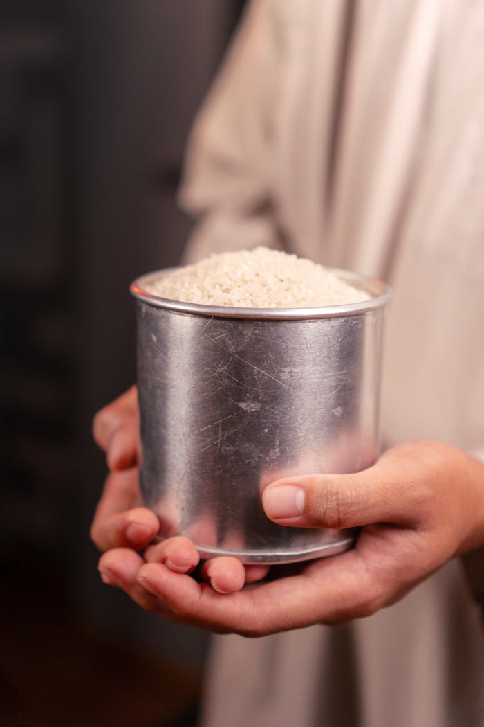 services-04 Close-up of hands holding a tin cup full of uncooked white rice, symbolizing abundance.